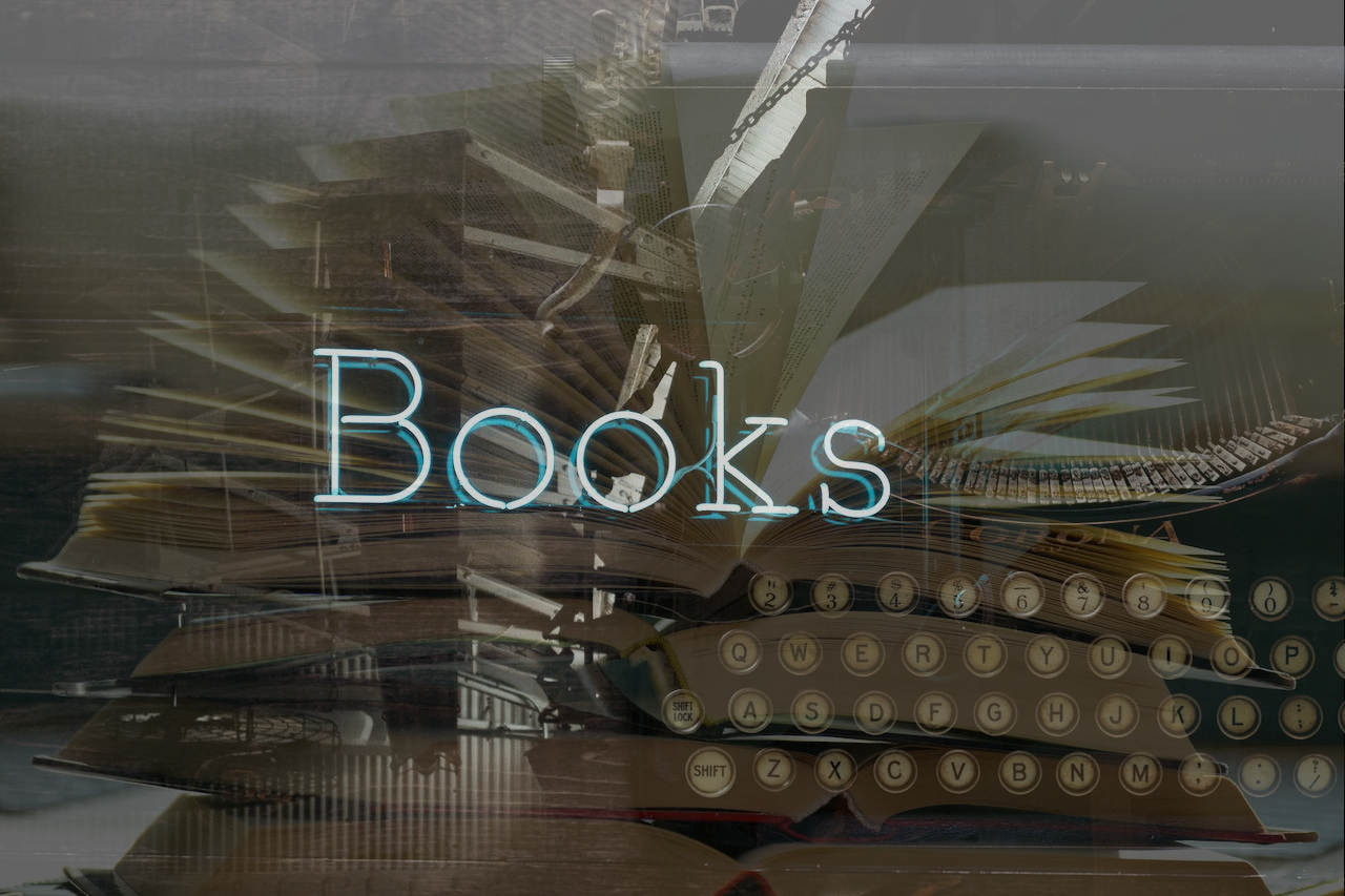 Imagen de un letrero luminoso de "Books" sobre una máquina de escribir antigua y un libro abierto.